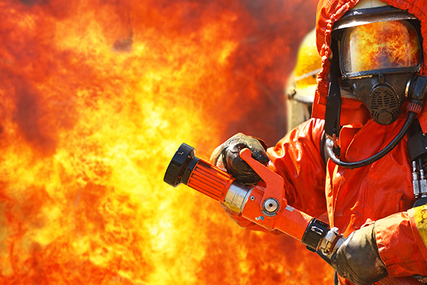 Bild: Feuerwehrmann in Hitzeschutzkleidung vor Feuerwand Bild: Feuerwehrmann in Hitzeschutzkleidung vor Feuerwand