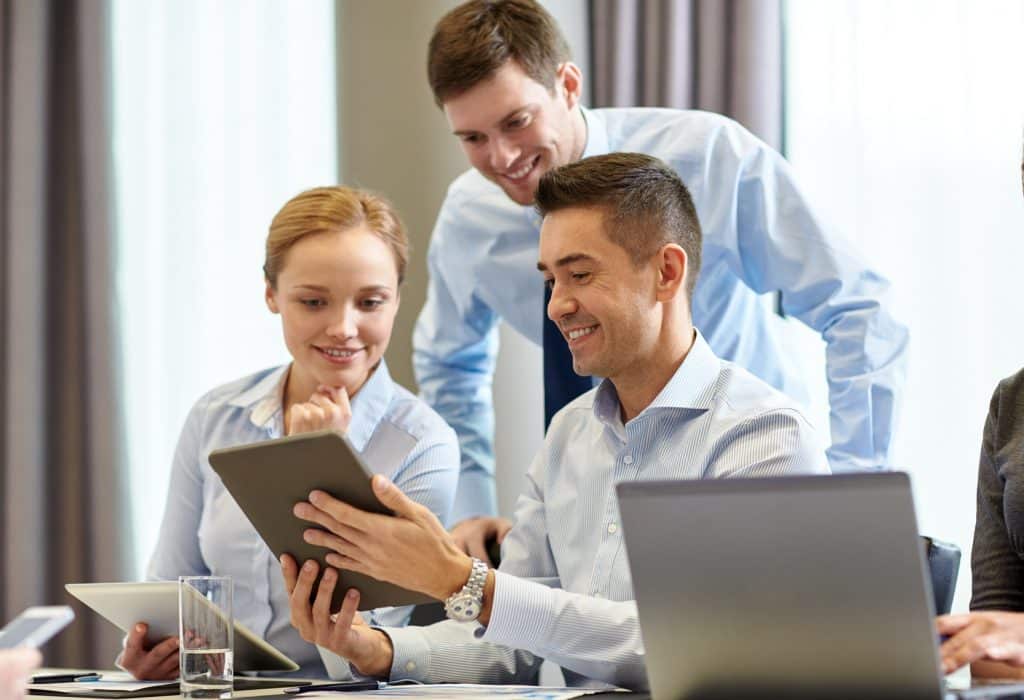 Bild: Menschen mit Laptop, business, people and technology concept - smiling business team with tablet pc computer meeting in office using microsoft teams