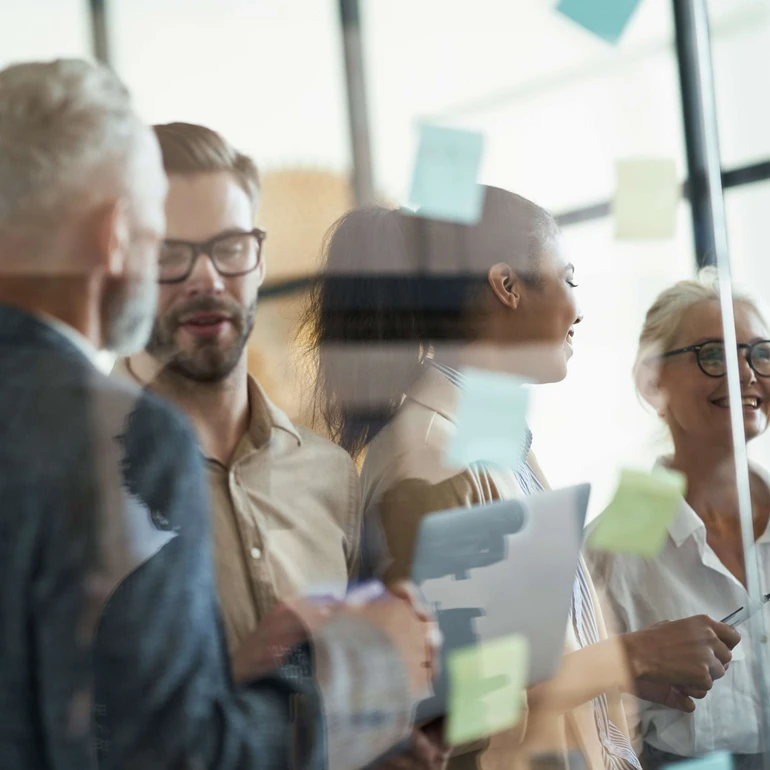 Mehrere Kolleginnen und Kollegen stehen vor Glaswänden mit Haftnotizen und besprechen Ideen.
