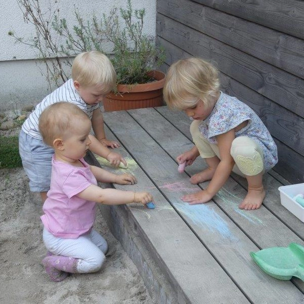 Drei Kleinkinder malen im Outdoorbereich mit Kreise auf den Holzboden