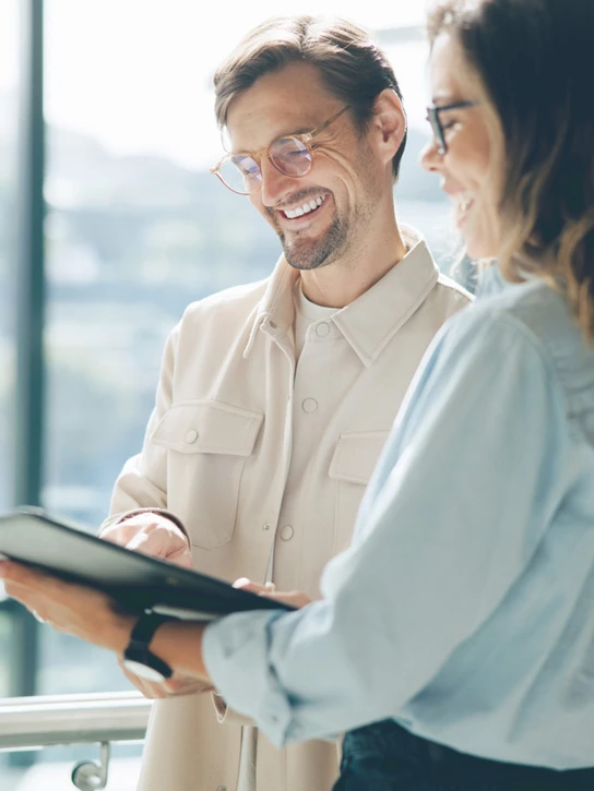Foto: Mann und Frau in heller Büroumgebung schauen auf Tablet