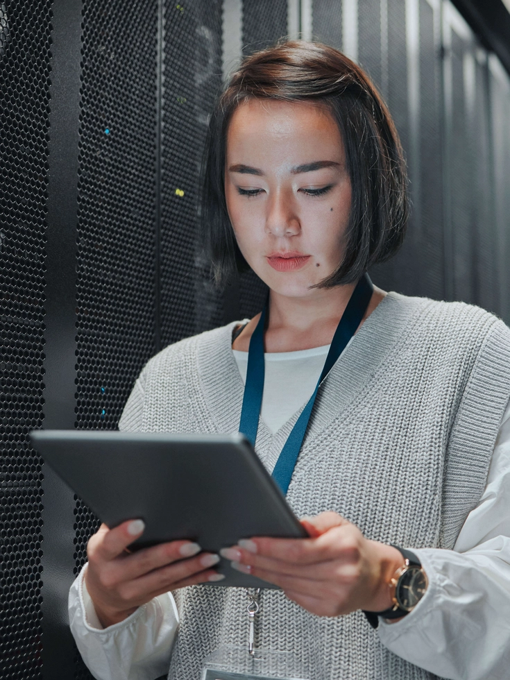 Technikerin arbeitet im Serverraum mit einem Tablet vor hochmodernen Rack-Systemen.