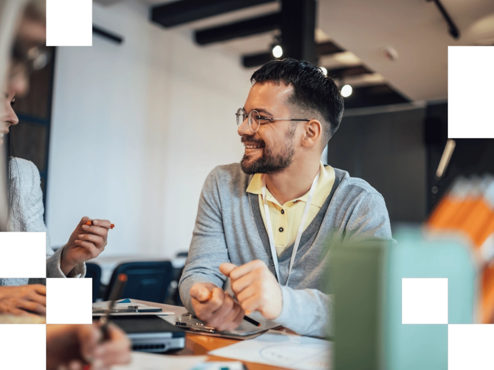 Lächelnder Mitarbeiter sitzt in einem Meeting und spricht mit Kolleginnen und Kollegen.