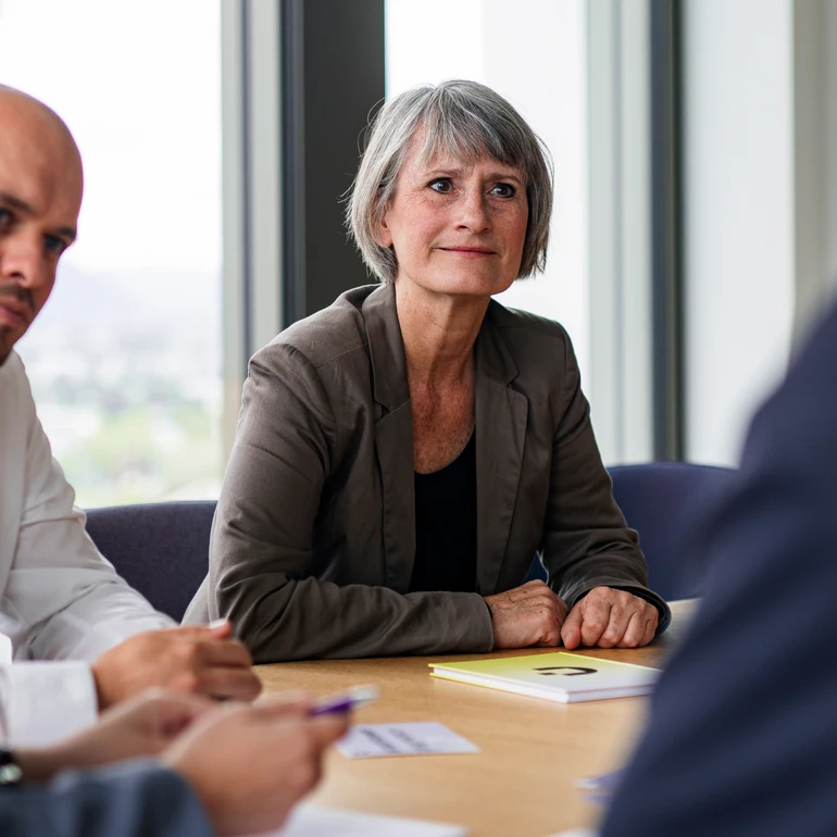 Frau in dunklem Shirt und braunem Blazer konzentriert und freundlich in einem Meeting