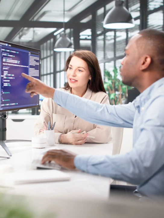 Foto: Kollege zeigt einer Kollegin Code auf einem Monitor