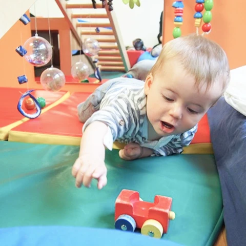 Kleinkind greift auf dem Bauch liegend nach einem Spielzeugauto