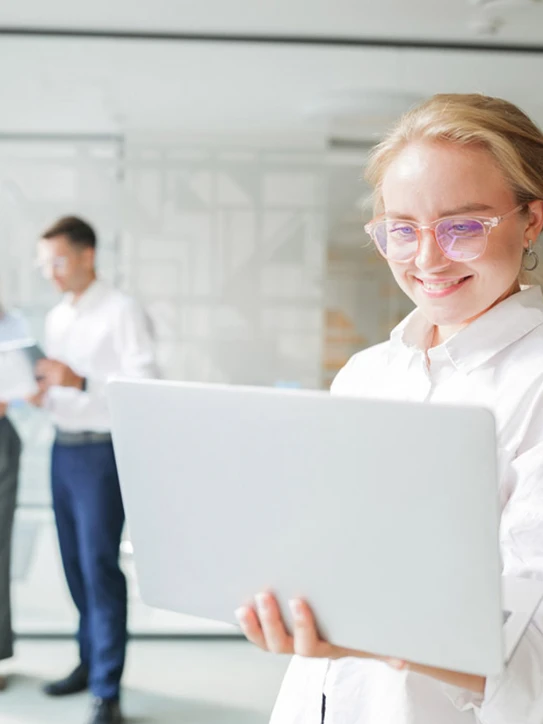 Foto: Stehende Frau im Büro hält geöffnetes Notebook in der Hand