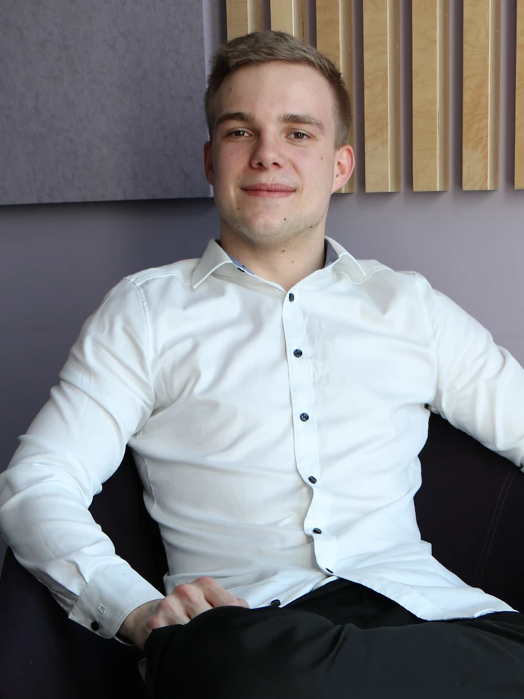 Portrait eines lächelnden, jungen conet Mitarbeiters in weißem Hemd in entspannter Büroumgebung