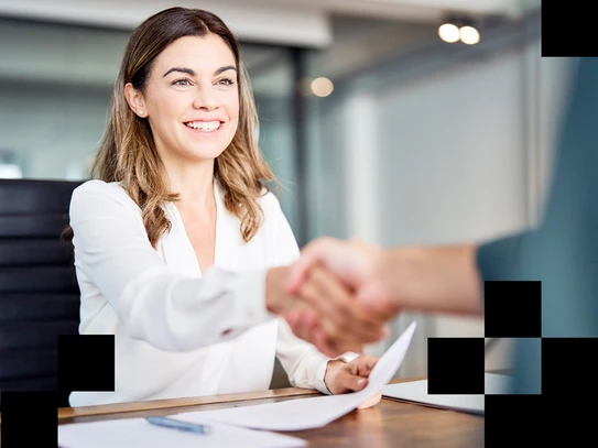 Foto: Frau sitzt am Tisch und reicht einer anderen Person die Hand