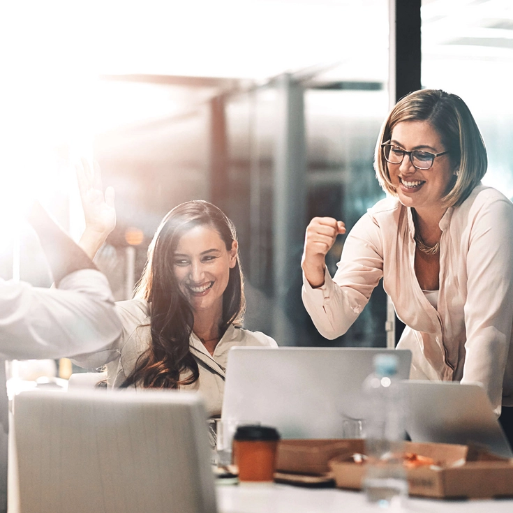 Gruppe von Mitarbeitenden jubelt und lacht während eines Meetings in einem modernen Büro.